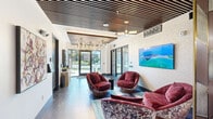 Located at 357 E 500 S in Salt Lake City, Utah, this thoughtfully designed residential lobby makes a strong first impression with its refined aesthetic and functional layout. The main lounge area is anchored by a curated seating arrangement of rich burgundy velvet swivel chairs set atop sculptural bases, positioned around a low coffee table atop a vibrant area rug — creating an inviting and stylish gathering space. A large flat-screen display is wall-mounted as a focal point, complemented by original artwork that adds color and personality to the space.

Overhead, a slatted wood ceiling with geometric detailing adds warmth and architectural depth, while contemporary chandelier lighting fixtures cast an ambient glow throughout. The flooring is finished in dark, veined marble-style tile that reinforces the upscale character of the space. Floor-to-ceiling glass doors at the entrance flood the lobby with natural light and offer views of the landscaped exterior.

The hallway transitions seamlessly into a dedicated package room, equipped with a full bank of LuxerOne smart package lockers — a convenient modern amenity for residents. An elevator provides access to upper floors, and curated wall art continues the design narrative throughout. Every detail of this lobby reflects a commitment to both elegance and everyday practicality.
