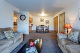 Located at 1215 Cannon View Dr in Grandview Plaza, Kansas, this single-floor residence offers a well-organized and functional layout designed for comfortable everyday living. The open-concept living and dining area forms the heart of the home, where plush carpeting, neutral walls, and ample space create a welcoming atmosphere. The living room features a sliding glass door that floods the space with natural light and provides direct access to a private outdoor patio with exterior views. A dedicated dining area comfortably accommodates a full dining set and includes a closeted storage area nearby. The galley-style kitchen is efficiently designed with white cabinetry, wood-look flooring, a full suite of appliances including a range, microwave, refrigerator, and dishwasher, and a pass-through counter that connects to the main living space. The bedroom offers carpeted flooring, a generously sized walk-in closet with built-in shelving, wall-mounted display shelves, and a window that allows natural light to filter in. The bathroom features wood-look flooring, a wide vanity with ample counter space and under-sink storage, and a decorative mirror. Throughout the residence, a consistent and cohesive design palette of warm neutrals and wood tones creates a practical and comfortable living environment.