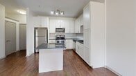 This 720-square-foot, two-bedroom, one-bathroom apartment is located at 4699 Kittredge Street in Denver, Colorado. The single-floor layout is designed for efficient use of space, connecting the kitchen and living area in an open arrangement. The kitchen is a standout feature, outfitted with white shaker-style cabinetry, dark granite countertops, a white subway tile backsplash, a central island, and a full suite of stainless steel appliances including a refrigerator, electric range, over-the-range microwave, and dishwasher. Rich hardwood-style flooring runs through the kitchen and living areas. The living room is bright and open, highlighted by French doors that open to a private balcony with outdoor views, allowing ample natural light. The primary bedroom measures 150 square feet and features plush carpeting, a ceiling fan, and a double-door closet. The second bedroom also offers carpeted flooring and built-in shelving with a desk nook beneath a large window. The bathroom is finished with dark gray subway tile wainscoting, wood-style flooring, a white vanity with a dark countertop, and a well-lit mirror. Three hallways and an additional closet complete the functional layout of this well-appointed Denver apartment.