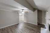 This two-story home in Houston, Texas offers a well-organized layout across two levels, combining functional design with comfortable living spaces. The main level hosts the kitchen and living area, while the upper level accommodates the bedrooms and bathrooms.

The living room is a standout space, featuring vaulted ceilings, a wood-style fireplace with a white tile surround and classic mantel, and durable hardwood-style flooring. A ceiling fan adds to the room's comfort, and the open sightlines create a welcoming atmosphere.

The galley-style kitchen is efficiently designed, with warm wood cabinetry lining both sides, granite-look countertops, a single-basin sink with a matte black faucet, and black appliances including a refrigerator, stove, microwave, and dishwasher. Light wood-style flooring and overhead lighting complete the space.

Each bedroom features plush carpeting, a ceiling fan, and natural light from windows. The generously sized primary bedroom includes direct access to an en-suite bathroom with a wood-toned vanity, large mirror, and a tub-shower combination finished in crisp white tile. The second bathroom is similarly appointed.

Both closets are walk-in style with built-in shelving and hanging rods, offering excellent storage. The home's neutral color palette and consistent finishes throughout create a cohesive and move-in-ready environment.