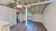 Located at 601 Bridge St in Danville, Virginia, this 2-bedroom, 1-bathroom residence showcases a distinctive architectural character that sets it apart. The open-concept living, dining, and kitchen area is the heart of the home, highlighted by dramatic exposed beam ceilings with white-painted wood planking, large skylights that flood the space with natural light, and durable wood-look flooring throughout. A ceiling fan and visible ductwork add an industrial-loft aesthetic to the airy main living area, which also features a central support column as a structural design element.

The kitchen is well-appointed with warm wood cabinetry, white countertops, stainless steel appliances including an electric range, microwave, and refrigerator, and a double-basin sink set into a peninsula that opens to the living space. Pendant lighting above adds a polished touch.

The primary bedroom is generously sized and benefits from the same soaring ceiling design and natural skylight illumination. The second bedroom offers additional flexibility. Four closets provide ample storage throughout the unit, complemented by an in-unit laundry area for added convenience.

The bathroom features a walk-in shower with tiled surround, a built-in bench, and a handheld showerhead. Wood-look flooring continues throughout, tying the space together cohesively.
