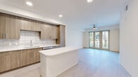 This thoughtfully designed one-bedroom, one-bathroom residence in Altamonte Springs, FL offers a clean, contemporary aesthetic throughout its efficiently organized single-floor layout. Light-toned luxury vinyl plank flooring runs seamlessly through the open-concept living, dining, and kitchen area, creating a bright and cohesive feel enhanced by recessed lighting and a ceiling fan overhead.

The kitchen is a standout feature, showcasing flat-front warm wood cabinetry extending to the ceiling, a subway tile backsplash, crisp white countertops, a central island with additional seating space, and a full suite of stainless steel appliances. The living area flows effortlessly toward floor-to-ceiling sliding glass doors that open onto a private balcony, offering serene views of a landscaped courtyard with palm trees and lush greenery.

The bedroom is well-proportioned, featuring a large window that frames outdoor courtyard views and fills the room with natural light. A dedicated closet provides convenient storage. The bathroom presents a refined finish with marble-look tile flooring, a wood-tone vanity with white countertop, a glass-enclosed walk-in shower, and clean modern fixtures. Additional spaces include a laundry area and utility room, rounding out this well-appointed residence.