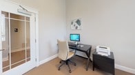 Located at 100 Bartons Run Trce in Lebanon, Tennessee, this single-floor office space offers a clean, professional environment designed for productivity and comfort. The room features neutral gray walls, plush carpeted flooring, and crisp white trim and baseboards that lend a polished, cohesive aesthetic throughout.

Natural light is a defining characteristic of this space, with multiple windows fitted with white horizontal blinds that allow for adjustable illumination while offering views of the surrounding exterior. The windows are framed with classic white molding, adding a refined architectural detail to the room.

A dedicated workstation area is equipped with a sleek dark desk paired with a modern ergonomic chair, a desktop computer, keyboard, and printer — providing all the essentials for an efficient work environment. Framed wall art above the desk adds a touch of personality to the otherwise minimalist setup.

A cozy reading or waiting nook is positioned near one of the windows, featuring a patterned accent chair and a side table with a lamp, creating an inviting corner ideal for informal meetings or relaxed moments.

Access to the space is through a distinguished glass-paneled interior door with white trim and a door closer, offering both visibility and a sense of openness. The overall ambiance is bright, calm, and functional — well-suited for professional use.