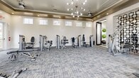 This state-of-the-art fitness center, located at 12020 Southern Highlands Parkway in Las Vegas, spans 1430 square feet on a single floor. The space is thoughtfully divided into distinct zones for various exercise modalities. The facility boasts an impressive array of equipment, including treadmills, ellipticals, weight machines, free weights, and stationary bikes. Large windows flood the area with natural light, creating an inviting atmosphere. The interior design features a sleek, modern aesthetic with white brick walls, gray patterned flooring, and elegant lighting fixtures, including eye-catching starburst chandeliers. High ceilings and strategically placed mirrors enhance the sense of spaciousness. The center incorporates functional training areas with equipment like TRX straps and medicine balls. Multiple flat-screen TVs are mounted throughout, providing entertainment during workouts. The layout promotes easy navigation and efficient use of space, catering to both individual exercisers and small group activities. Overall, this fitness center offers a comprehensive and visually appealing environment for health and wellness pursuits.