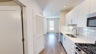 This efficiently designed studio unit offers a well-organized single-floor layout that maximizes every square foot. The open main living area features wood-style plank flooring and crisp white walls, creating a bright and clean aesthetic. A large window allows natural light to fill the living space, offering views of the surrounding exterior and balcony areas nearby.

The kitchen is a standout feature, outfitted with sleek white cabinetry extending to the ceiling, white quartz-style countertops, and a subway tile backsplash. Stainless steel appliances include a gas range, over-the-range microwave, dishwasher, and a full-size refrigerator, providing a fully functional cooking space. Recessed and track lighting illuminate the kitchen and entry corridor effectively.

A louvered door leads to a closet off the main hallway, while the full bathroom is well-appointed with a wood-toned vanity, undermount sink, wood-style tile flooring, and a shower-tub combination with tiled surround. Accessibility grab bars are thoughtfully installed. The unit also features a recessed electrical panel along the hallway wall. The overall design is modern and neutral, offering a clean, move-in-ready environment with practical finishes throughout.