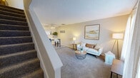 Located at 6741 C Avenue NE in Cedar Rapids, Iowa, this two-story home offers a practical and comfortable layout across two evenly sized floors. The main level features a carpeted living room filled with natural light from a large window dressed with sheer vertical blinds, creating a warm and welcoming atmosphere. A staircase with white railings connects seamlessly to the dining area, which is served by a galley-style kitchen. The kitchen includes wood-trimmed cabinetry, white appliances, a double-basin sink, and durable hardwood-style flooring, maximizing efficiency in a compact space. A bathroom on this level features hardwood-style flooring, a vanity, and a shower-tub combination. Upstairs, the spacious primary bedroom offers plush carpeting, a large window with vertical blinds, and ample room for furnishings. Two additional bedrooms share the upper floor, each with carpet flooring and natural light. The second full bathroom upstairs includes a vanity, toilet, and a shower with a decorative curtain. Throughout the home, neutral warm-beige tones, textured ceilings, and consistent flooring choices create a cohesive and inviting aesthetic well-suited for everyday living.