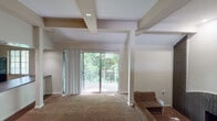 This single-floor residence offers a thoughtfully designed open-concept layout that blends functionality with architectural character. The living area serves as the heart of the home, featuring distinctive exposed ceiling beams that add visual depth and warmth to the space. Plush wall-to-wall carpeting runs throughout, complementing the neutral, light-toned walls. A standout feature is the sliding glass door that opens to a private balcony, framing lush greenery beyond and allowing abundant natural light to fill the room. A brick accent wall with a hearth adds texture and a focal point to the living space.

The kitchen is efficiently designed with a pass-through counter that connects it visually to the main living area, promoting an open flow. White cabinetry, dark granite-style countertops, black appliances, and hardwood-style flooring complete the kitchen's clean and practical aesthetic. A window above the counter brings in additional natural light.

The bathroom is well-appointed with a single vanity, under-sink storage, a combined tub and shower, and hardwood-style flooring that echoes the kitchen. A large mirror and wall-mounted lighting enhance the sense of space. Throughout the residence, the consistent use of neutral tones and natural light creates a cohesive, inviting ambiance.
