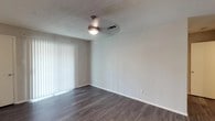 This single-floor residence offers a clean, modern aesthetic carried consistently throughout its thoughtfully designed layout. Rich, dark hardwood-style flooring flows across the living areas and bedrooms, providing a warm contrast to the neutral gray and white walls that brighten each room.

The open living area is generously sized, bathed in natural light streaming through large sliding glass doors dressed with vertical blinds. A ceiling fan with a light fixture adds both comfort and functional illumination to the space. A low interior dividing wall adds architectural interest, subtly defining areas while maintaining an open feel.

The kitchen is a standout feature, offering dark espresso cabinetry paired with light quartz-style countertops and a gray tile backsplash. Stainless steel and black appliances — including a refrigerator, electric range, and over-the-range microwave — lend a sleek, contemporary look to the efficient galley-style layout.

The bedrooms are well-proportioned, each featuring the same durable flooring, ceiling fans, and windows with blinds that allow for natural light and privacy. Textured ceilings are present throughout the unit, adding subtle dimension overhead.

The bathroom is finished with crisp white square tile surrounding a full soaking tub and shower combination, offering a clean and classic aesthetic. Overall, the space presents a cohesive, move-in-ready environment with modern finishes and practical design throughout.