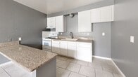 Located at 12035 White Ave in Adelanto, CA, this single-story, one-bedroom, one-bathroom home offers a practical and efficient layout. The open-concept main area seamlessly combines the living room, dining space, and kitchen into one cohesive zone, finished with large-format light tile flooring that runs throughout the entire home. The kitchen is well-equipped with white shaker-style cabinetry — both upper and lower — granite-patterned countertops, a peninsula with additional counter space, a gas range with overhead ventilation, and a single-basin sink. A textured ceiling adds architectural character to the main living area. The bedroom is a comfortable size, featuring a sliding-door closet, tile flooring consistent with the rest of the home, and a window fitted with vertical blinds that allows natural light to enter. The bathroom includes a full shower-tub combo with a curtain rod, a toilet, and tile flooring. A hallway connects the main living area to the bedroom and bathroom, completing the straightforward and functional floor plan. The home's consistent gray wall palette and white trim give the interior a clean, cohesive appearance throughout.
