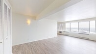 Located at 740 Mississippi River Blvd S in Saint Paul, Minnesota, this well-appointed unit offers a clean, modern aesthetic throughout its single-floor layout. The open living area is bathed in natural light streaming through large floor-to-ceiling windows, which frame sweeping panoramic views of the surrounding landscape — a standout feature of the space. Light wood-toned flooring runs throughout, complementing the bright white walls and creating an airy, cohesive feel. A wall sconce adds a warm accent to the generous living area, which also features a baseboard heating unit beneath the windows.

The kitchen is thoughtfully designed with white cabinetry extending to the ceiling, granite-style countertops, a mosaic tile backsplash, and white appliances including a refrigerator, electric range, built-in microwave, and sink. Track lighting overhead ensures the workspace is well-illuminated.

The bedroom is spacious and serene, featuring a full wall of louvered bi-fold closet doors for ample storage. It connects to a dedicated walk-in closet area with built-in shelving and hanging rods on both sides, which in turn leads directly to the bathroom. The bathroom is finished with classic white tile, a tub-shower combination with an overhead rain-style showerhead, and a recessed mirrored medicine cabinet.