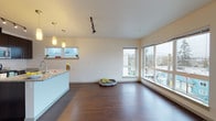 Located in Seattle's vibrant Ballard neighborhood, this single-floor residence at 1139 NW Market Street offers a thoughtfully designed open-concept layout with modern finishes throughout. Rich hardwood-style flooring flows through the main living areas, complemented by clean white walls and contemporary track lighting.

The kitchen is a standout feature, showcasing dark espresso cabinetry, granite countertops, a stainless steel appliance suite including a range, microwave, and refrigerator, and a central island with pendant lighting overhead. The kitchen opens seamlessly to the living area, which is bathed in natural light through expansive floor-to-ceiling windows offering sweeping views of the Seattle skyline and surrounding neighborhood.

The bedroom is carpeted for comfort and features a large window with continued city views, providing an airy and bright atmosphere. Two bathrooms serve the unit — one featuring a granite-topped vanity with dark cabinetry and hardwood-style flooring, and the other offering a full tub-shower combination with a curved curtain rod and matching finishes. Both bathrooms maintain a clean, modern aesthetic consistent with the rest of the home. The overall ambiance is bright, contemporary, and well-suited for urban living in one of Seattle's most walkable districts.