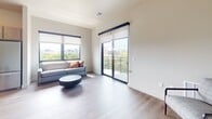 This well-designed 820-square-foot apartment offers 2 bedrooms and 2 bathrooms across a single floor, combining modern aesthetics with functional living. The open-concept kitchen and living area serves as the heart of the unit. The kitchen is equipped with stainless steel appliances—including a refrigerator, range, microwave, and dishwasher—complemented by light gray shaker-style cabinetry, white quartz countertops, a classic subway tile backsplash, and rustic wood floating shelves. A pendant light fixture adds a warm, stylish accent above the dining area. The living room is bright and airy, featuring large black-framed windows and a sliding glass door that opens to a private balcony with sweeping city and treetop views. Wood-look flooring runs throughout the unit, adding warmth and cohesion. The primary bedroom measures 150 square feet and includes a large window with urban views. The second bedroom also features a generous window with an elevated city outlook. Both bathrooms are finished consistently with gray vanities, white quartz countertops, chrome fixtures, and tub-shower combinations. Neutral wall tones and clean lines give the entire unit a bright, contemporary ambiance.