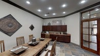 Located along Long Prairie Trace in Richmond, Texas, this single-story space presents a cohesive rustic-modern interior anchored by striking slate tile flooring that runs throughout. The main gathering area is generously proportioned, accommodating a substantial wood dining table surrounded by slatted wood chairs, making it well-suited for meetings or group gatherings.

Dark espresso-toned cabinetry lines one wall, offering ample upper and lower storage with a continuous countertop surface ideal for serving or workspace. Recessed lighting is installed throughout the ceiling, providing consistent, even illumination across the interior. Bold dark crown molding frames the ceiling perimeter, adding architectural definition and contrast against the neutral light gray walls.

A set of wood-framed French doors with glass panels serves as a prominent architectural feature, connecting the interior to an adjacent space while allowing natural light to filter through. A large window fitted with wood blinds further brightens the room and provides views to the outdoors. Decorative wall medallions and metalwork accents contribute to the space's industrial-rustic character. A rustic wood sideboard along one wall adds additional storage and display functionality, completing the well-appointed interior.