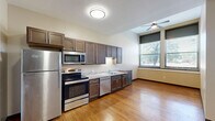 Located at 510 E Washington St in Bloomington, Illinois, Unit 108 is a thoughtfully designed one-bedroom, one-bathroom residence that makes efficient use of its single-floor layout. The kitchen is a functional highlight, featuring rich dark wood cabinetry, granite-style countertops, and a full suite of stainless steel appliances including a refrigerator, electric range, microwave, and dishwasher. Warm hardwood flooring extends throughout the kitchen and main living areas, adding character and a sense of warmth. A distinctive decorative glass entry door with a transom window lends a charming, historic touch to the space. The bedroom is comfortably sized, carpeted for comfort underfoot, and features tall ceilings that enhance the sense of openness. Large windows with views of mature trees fill the room with natural light and provide pleasant outdoor scenery. The bathroom is clean and practical, equipped with a full bathtub and shower combo, light wood-look tile flooring, and accessibility grab bars for added safety and convenience. A connecting hallway ties the rooms together seamlessly. Overall, the unit offers a balanced mix of classic architectural details and modern finishes in a convenient Bloomington location.