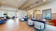 This well-appointed single-story community clubhouse offers an expansive and thoughtfully designed layout across a generous footprint. The entrance greets visitors with a sleek reception area featuring dark countertop workstations, warm wood-plank flooring, elegant pendant lighting, and a distinctive herringbone-patterned wood accent wall — creating a polished, professional first impression. Decorative geometric mirrors add a contemporary artistic touch to the reception space.

Connected hallways lead to a spacious living room bathed in natural light from large floor-to-ceiling windows that frame outdoor views of the community pool and surrounding landscape. Soaring vaulted ceilings with exposed wood beam accents lend an airy, open ambiance, while comfortable seating arrangements, a wall-mounted television with built-in display niches, and an exposed brick accent wall contribute warmth and character.

The dedicated exercise room is a standout feature, boasting a vibrant teal tray ceiling, ceiling fans, full-length mirrors, and broad windows overlooking the pool area. It is outfitted with a comprehensive selection of fitness equipment, including weight machines, treadmills, ellipticals, and cycling machines, all set on durable patterned carpet tile flooring. Three connecting hallways ensure smooth circulation throughout the entire facility.