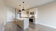 This single-floor space showcases a thoughtfully designed, modern interior with a cohesive neutral color palette and high-quality finishes throughout. The open-concept kitchen serves as the centerpiece of the unit, featuring a central island with a white quartz countertop and built-in storage, paired with two striking matte black pendant lights overhead. Cabinetry combines crisp white upper cabinets with light wood lower cabinets, while a classic white subway tile backsplash runs along the walls. Stainless steel appliances, including a gas range, built-in microwave, and French door refrigerator, complete the functional yet stylish kitchen. Dark hardwood-style flooring flows throughout the main living areas, providing a warm contrast to the light walls and cabinetry.

The bedroom offers a quiet retreat with soft, neutral carpeting and clean, minimalist walls. The bathroom is well-equipped with a white quartz vanity countertop, undermount sink, matte black hardware, a framed rectangular mirror, and ample drawer storage. An adjacent walk-in closet with wire shelving adds practical storage. The overall ambiance of the space is clean, modern, and move-in ready.