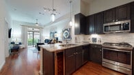 This single-story residence offers a well-appointed open-concept layout that seamlessly connects the kitchen, dining, and living areas. The kitchen is a standout feature, showcasing dark espresso cabinetry extending to the ceiling, granite countertops, a tile backsplash, stainless steel appliances including a gas range, built-in microwave, and refrigerator, and a peninsula with bar seating illuminated by modern pendant lighting. Track lighting above adds further functionality to the space.

The dining area comfortably accommodates a full table and flows naturally into the living room, where hardwood flooring, a tray ceiling, and a ceiling fan contribute to a polished atmosphere. A large sliding glass door floods the living area with natural light and opens to a private balcony with outdoor views.

The bedroom is a serene retreat featuring plush carpet, a generously sized window with greenery views, and ample natural light filtered through sheer curtains. The bathroom is elegantly finished with large-format marble-look tile on both the floors and shower walls, a glass-enclosed shower, and a vanity with stone countertops, creating a refined, spa-like environment throughout.