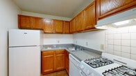 This single-floor residence offers a practical and straightforward layout, as revealed by the available floor plan. The kitchen is equipped with warm oak cabinetry extending to the upper walls, providing generous storage capacity. Granite-speckled laminate countertops form an L-shaped workspace that includes a stainless steel sink, a gas range, a dishwasher, and a full-size refrigerator. Light hardwood flooring grounds the kitchen, adding warmth to the space.

The living area is notably spacious, featuring neutral wall-to-wall carpeting and white walls that create a bright, open atmosphere. A chandelier serves as a focal point in the dining area, while a large sliding glass door fitted with vertical blinds allows natural light to pour in and provides access to an outdoor area. The generous proportions of the living space accommodate a variety of furniture arrangements.

The bedroom is well-sized, carpeted, and features a window with an outdoor view, along with two side-by-side closets offering ample storage with built-in shelving and hanging rods. The full bathroom includes white ceramic tile flooring, a tiled tub-shower combination, a vanity with wood cabinetry, and clean, neutral finishes throughout.