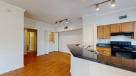This single-floor residence offers a thoughtfully designed layout with a welcoming open-concept living and kitchen area. Warm hardwood flooring flows throughout the main living spaces, complemented by crown molding and crisp white walls that create a clean, polished aesthetic. The living room is bathed in natural light from large windows fitted with blinds, and a ceiling fan adds comfort to the generous, open space.

The kitchen is well-equipped with warm-toned wood cabinetry, dark granite-style countertops, stainless steel appliances, and a track lighting system overhead. A peninsula with a built-in sink and breakfast bar connects the kitchen to the living area, offering both functionality and an inviting layout for entertaining. Tile flooring in the kitchen provides a practical transition from the hardwood of the main living space.

A dedicated in-unit laundry area with stacked washer and dryer is conveniently tucked behind bifold doors. The bedroom features plush carpeting, a ceiling fan, and a large window that allows natural light to fill the room. The bathroom includes warm wood cabinetry with granite-style countertops, tile flooring, and access to a walk-in closet, rounding out this functional and comfortable residence.