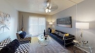 This single-floor residence offers a thoughtfully designed layout across several distinct living areas. The living room serves as the central gathering space, featuring carpet flooring, a ceiling fan with light fixture, and a sliding glass door dressed with vertical blinds that allows natural light to fill the room. The neutral gray walls provide a versatile backdrop throughout the unit.

The galley-style kitchen is efficiently organized with white cabinetry, dark granite-look countertops, and wood-look flooring. Black appliances, including a refrigerator, electric range, and dishwasher, are complemented by ample upper and lower cabinet storage.

Adjacent to the kitchen, the dedicated dining area features the same wood-look flooring and offers comfortable space for a four-seat table setting beneath a flush-mount ceiling light.

The two bedrooms are carpeted and each includes a ceiling fan, window with natural light, and closet access. Both bathrooms are finished consistently with white cabinetry, dark countertops, large mirrors with vanity lighting, wood-look flooring, and shower-tub combinations with curtains. Each bathroom also features louvered cabinet doors for additional storage.