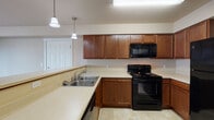 Located at 802 South Garfield Road in Airway Heights, Washington, Unit 106 is a single-floor residence designed for comfortable, functional living. The open-concept living area is generously sized, featuring warm neutral-toned walls, plush carpeting, and multiple windows that invite natural light throughout the day. A private exterior door provides direct outdoor access, adding convenience and a welcoming entry point to the unit. The kitchen is well-appointed with rich wood cabinetry, light countertops, and a full suite of black appliances including an electric range, over-the-range microwave, refrigerator, and dishwasher. Pendant lighting and tile flooring complete the kitchen's practical yet inviting aesthetic. A breakfast bar-style counter connects the kitchen to the living space, enhancing the open feel. A dedicated pantry closet with built-in shelving provides ample storage. The bathroom features a vanity with wood cabinetry and tile flooring, and is conveniently situated adjacent to an in-unit laundry area equipped with a full-size washer and dryer. The bedroom offers carpeted flooring, a window with exterior views, and closet access. Throughout the unit, the design emphasizes functionality and ease of living in a well-maintained residential setting.