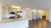 Located at One Third Avenue in Mineola, New York, this modern residence offers a clean, contemporary design throughout its single-floor layout. Rich dark hardwood flooring flows seamlessly across the open-concept living and dining area, creating a warm contrast against the crisp white walls and smooth ceilings. Large windows invite generous natural light into the living area, offering views of the surrounding neighborhood. The open kitchen is thoughtfully designed with light wood cabinetry, stainless steel appliances including a gas range, built-in microwave, and French door refrigerator, all centered around a white island with an undermount sink. A tall pantry cabinet with frosted glass sliding doors adds both style and practicality to the kitchen space. The bedrooms are bright and well-proportioned, each featuring dark hardwood floors, neutral walls, and ample closet storage with built-in shelving and hanging rods. Two bathrooms serve the residence: one features a walk-in shower with floor-to-ceiling tile and a gray vanity, while the second includes a full soaking tub with shower, matching vanity, and tile flooring. The overall ambiance is clean, modern, and move-in ready, well-suited for comfortable everyday living.