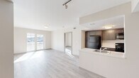 This 2-bedroom, 2-bathroom residence is thoughtfully designed with a clean, modern aesthetic throughout. The open-concept living and kitchen area serves as the heart of the home, featuring light wood-style flooring that flows seamlessly across the entire floor. The kitchen is equipped with dark espresso cabinetry reaching to the ceiling for ample storage, black appliances including a refrigerator, gas range, and microwave, and a light-toned peninsula countertop with an integrated sink — ideal for both meal prep and casual dining. The living room is bright and airy, receiving abundant natural light through large sliding glass doors that open onto a private balcony overlooking the surrounding neighborhood. A teal accent entry door adds a distinctive touch upon arrival, with track lighting enhancing the open hallway and living space. The primary bedroom offers a comfortable footprint with a large window framing outdoor views and generous wall space. The second bedroom is equally well-lit and functional. Both bathrooms are finished with neutral tones; one features a walk-in shower with chrome fixtures, while the other includes a full soaking tub/shower combination with hexagonal tile flooring and dark vanity cabinetry. A connecting hallway provides easy access to all rooms, contributing to the unit's efficient and livable layout.