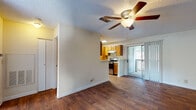 This single-story 1-bedroom, 1-bathroom unit offers a practical and comfortable layout with consistent wood-style flooring flowing throughout the main living areas. The open living room is spacious and bright, featuring a ceiling fan with light fixture, a textured ceiling, and neutral-toned walls that create a clean, versatile backdrop. Vertical blinds frame a sliding glass door that opens directly onto a private balcony, providing natural light and outdoor views of surrounding greenery.

The galley-style kitchen is efficiently arranged with warm honey-toned wood cabinetry, ample upper and lower storage, a double-basin sink with white countertops, and stainless steel appliances including a range and refrigerator. A pass-through counter connects the kitchen to the living area, enhancing the open feel of the space.

The bedroom is a well-proportioned, quiet retreat with plush carpeting, a large window with outdoor views, and a textured ceiling with overhead lighting. A closet provides convenient built-in storage.

The full bathroom includes a tub/shower combination with white tile surround, a wood-framed vanity with a single sink, a large mirror with overhead vanity lighting, and wood-style flooring that ties the space together cohesively.