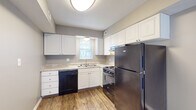 Located at 5028 Dierker Rd in Columbus, Ohio, this two-floor residence offers a well-organized layout across both levels. The kitchen is equipped with white shaker-style cabinetry, light granite-look countertops, a double-basin sink, and stainless steel appliances including a gas range and refrigerator, complemented by a black dishwasher and durable hardwood-style vinyl flooring. Natural light filters in through a window fitted with blinds. The main living area features the same hardwood-style flooring and a large sliding glass door with vertical blinds that opens to an outdoor space, filling the room with ample natural light. A carpeted staircase with a wood and metal railing connects the two floors. The bedrooms are finished with plush carpeting and neutral-toned walls; one bedroom features dual windows for added brightness, while another includes built-in shelving, hardwood-style flooring, and convenient storage. The bathroom is outfitted with a full tub and shower surround with integrated shelving, brushed nickel fixtures, and matching hardwood-style flooring. Throughout the home, a consistent neutral color palette and clean finishes create a cohesive and functional living environment.