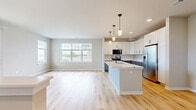 Located at 1211 Carrington Blvd in Mount Pleasant, WI, this 890-square-foot, single-floor unit offers a clean, modern aesthetic with high-quality finishes throughout. The open-concept kitchen and living area serves as the heart of the home, featuring light hardwood-style flooring that flows seamlessly through the main living spaces. The kitchen is well-appointed with white upper shaker cabinets, contrasting gray lower cabinets, stainless steel appliances including a range, microwave, and refrigerator, and a large center island with a white quartz countertop and undermount sink — ideal for both cooking and entertaining. The living room is bright and airy, with a sliding glass door leading to a private balcony and additional windows offering neighborhood views and abundant natural light. The 170-square-foot primary bedroom features plush carpet, a large window with outdoor views, and access to a walk-in closet with wire shelving for organized storage. The full bathroom is finished with light wood-look flooring, a gray vanity with a white countertop, a tub-shower combination, and matte black hardware and fixtures throughout. Neutral wall tones and clean white trim unify the space with a contemporary, move-in-ready appeal.