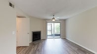 This single-story unit is designed with a neutral, modern aesthetic and consistent wood-style flooring that runs throughout the main living areas and bedrooms. The spacious living room serves as the focal point of the unit, anchored by a tiled fireplace and bathed in natural light from a full-width sliding glass door that opens to a private balcony overlooking greenery. A ceiling fan with a light fixture adds both function and visual appeal to the space.

The kitchen is a well-appointed galley layout featuring white cabinetry, light stone-look countertops, stainless steel appliances including a refrigerator, dishwasher, and electric range, and a double-basin sink. A pass-through opening connects the kitchen to the adjacent living and dining area, enhancing the sense of openness.

The bedrooms are comfortably sized with neutral gray walls, wood-style flooring, and window blinds that allow for adjustable natural light. One bedroom includes a ceiling fan. The bathrooms feature white tile surrounds in the tub and shower areas, a vanity with stone-look countertops, and a large mirror, all finished in a clean, functional style. Textured ceilings are present throughout the unit.