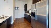 Located at 18 Mechanic St in Quincy, Massachusetts, this single-floor unit showcases a contemporary design aesthetic defined by polished, stained concrete floors that run throughout the entire space, lending a distinctive industrial-modern character. The layout is thoughtfully organized, with distinct areas for living, cooking, and bathing.

The living and main areas benefit from large, black-framed windows that flood the rooms with abundant natural light while offering pleasant views of the surrounding neighborhood, including mature trees and nearby rooftops. Clean white walls provide a neutral backdrop that complements the rich, dark tones of the flooring.

The kitchen is well-appointed with a two-tone cabinetry scheme—dark lower cabinets contrasted by crisp white upper cabinets—paired with light countertops and a full suite of stainless steel appliances, including a gas range, built-in microwave, dishwasher, and refrigerator. Recessed lighting illuminates the kitchen and open living area effectively.

The bathroom is cleanly finished, featuring a full soaking tub with a tiled surround, a toilet, and a vanity, all set against white walls and the same polished concrete flooring found throughout the unit. The overall ambiance is modern, minimal, and move-in ready.