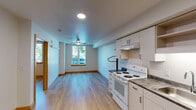 Located at 12370 SE Ash St in Portland, Oregon, this single-floor unit offers a clean, functional layout designed for comfortable everyday living. Light-toned luxury vinyl plank flooring runs throughout the main living areas, complementing the bright, neutral-painted walls and warm wood baseboards that give the space a cohesive, modern feel.

The kitchen is well-equipped and efficient, featuring light wood cabinetry with gold-toned hardware, ample upper and lower storage, open display shelving, a double-coil electric range, a full-size refrigerator, an under-cabinet range hood, and a stainless steel sink with a stone-look countertop. The kitchen flows openly into the living area, creating a connected, versatile space ideal for both cooking and relaxing.

The bedroom is a calm, well-proportioned room with smooth white walls, a ceiling fan with integrated lighting, warm wood baseboards, and a window that brings in natural light and views of the surrounding greenery.

The bathroom is neatly appointed with a single-basin vanity set in a stone-look countertop, light wood cabinetry below, a large mirror, chrome fixtures and grab bars, and a full shower-tub combo. Recessed and overhead lighting provides ample illumination throughout.

Overall, this unit presents a tidy, move-in-ready space with practical finishes and a straightforward, accessible design.
