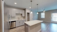 This well-appointed single-floor residence offers a thoughtfully designed layout that balances modern aesthetics with everyday functionality. The open-concept kitchen serves as the heart of the home, featuring gray shaker-style cabinetry, gleaming quartz countertops, a center island with pendant lighting, and a full suite of stainless steel appliances including a refrigerator, range, microwave, and dishwasher. A dedicated pantry provides generous additional storage. The kitchen flows seamlessly into a bright living area finished with wood-look luxury vinyl flooring and a ceiling fan, with natural light streaming in through a large window and access to an exterior door. A connecting hallway leads to the private areas of the home. The bedrooms are finished with plush wall-to-wall carpeting and ceiling fans, offering a comfortable retreat. One bedroom is accompanied by a spacious walk-in closet fitted with wire shelving for organized storage. Two full bathrooms serve the residence — one featuring a soaking tub with tile surround, and the other a glass-enclosed walk-in shower, both appointed with white vanities, quartz counters, and wood-look tile flooring. The neutral color palette and clean finishes throughout lend a cohesive, contemporary feel to the entire space.