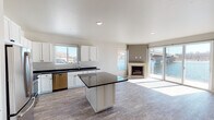 This contemporary two-floor waterfront property offers a striking blend of modern design and natural scenery. Light wood-tone flooring runs throughout, complementing the clean, neutral palette across both levels.

The main living area is anchored by an open-concept layout that seamlessly connects the kitchen and living room. Large sliding glass doors and expansive windows frame sweeping water views, flooding the space with natural light. A corner fireplace with a minimalist surround adds warmth and a focal point to the living area. The kitchen is thoughtfully designed with crisp white shaker cabinetry, dark granite countertops, a central island, and a full suite of stainless steel appliances including a refrigerator, range, microwave, and dishwasher.

The second floor mirrors similar quality, featuring an additional fully equipped kitchen with matching white cabinetry, granite surfaces, and stainless appliances. A spacious bedroom on this level opens directly to a private outdoor area overlooking the water, and is served by a generous walk-in closet with dual hanging systems. Bathrooms on both floors feature white vanity cabinetry, dark granite counters, and wood-look flooring — one includes a double-sink vanity. A dedicated laundry room with full-size washer and dryer adds everyday convenience.