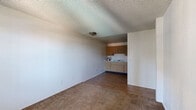 Located at 4201 N 35th Ave in Phoenix, Arizona, this two-bedroom, one-bathroom unit offers a practical and efficient single-floor layout. The living area is finished with wall-to-wall carpet and a textured ceiling, creating a straightforward, functional space that flows directly into the kitchen. The kitchen is equipped with warm-toned wood cabinetry spanning both upper and lower sections, a double-basin sink, electric range, and a full-size refrigerator, with dark hardwood-style flooring tying the space together. A compact hallway with light wood-style flooring and wall sconce lighting connects the main living area to the bedrooms and bathroom. Both bedrooms feature plush carpeting and textured ceilings; one bedroom includes a window unit air conditioner and entry door with a window, while the other offers a reach-in closet with a shelf rod. The shared full bathroom includes a single-sink vanity with light wood cabinetry, a large mirror, and a tiled tub-and-shower combination. Clean white walls throughout lend a neutral backdrop, making the space easy to personalize. The unit provides essential amenities in a compact, manageable footprint suited for everyday living in the Phoenix metro area.