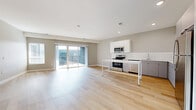 Located along State Line Road in Kansas City, KS, this well-designed one-bedroom, one-bathroom residence offers a thoughtfully planned open-concept layout across a single floor. Light-toned hardwood flooring flows throughout the main living areas, complementing the neutral gray walls and white trim that give the space a clean, modern aesthetic.

The combined kitchen and living area forms the heart of the home. The kitchen is outfitted with white upper cabinetry, gray lower cabinets, a white subway tile backsplash, light quartz countertops, and a full suite of stainless steel appliances including a range, microwave, dishwasher, and refrigerator. A freestanding island provides additional prep and dining space. The living area is generously sized and filled with natural light, anchored by sliding glass doors that open directly onto a private balcony.

The spacious bedroom features plush carpeting, a large window for natural light, and direct access to a walk-in closet equipped with built-in wire shelving across multiple walls. The bathroom continues the home's clean design with light hardwood-style flooring, a vanity with countertop storage, and a glass-enclosed walk-in shower. The overall ambiance throughout is bright, neutral, and move-in ready.