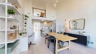 This thoughtfully designed residence makes a striking first impression with its dramatic double-height ceilings and expansive floor-to-ceiling windows that flood the interior with natural light. Light wide-plank hardwood flooring runs throughout, tying the open-plan layout together seamlessly.

The living area is anchored by the soaring ceiling height, with a lofted mezzanine level above accessible via railing, adding architectural depth and visual interest. Large steel-framed glass doors open directly to an outdoor terrace, blurring the boundary between indoor and outdoor living while providing generous views of the surrounding neighborhood.

The dining area centers on a natural wood table beneath a cluster of pendant lights, positioned adjacent to a dedicated workspace with open white shelving. The kitchen is outfitted with light shaker-style cabinetry, quartz countertops, a subway tile backsplash, and a full suite of stainless steel appliances. A butcher block island with bar seating provides additional prep and casual dining space.

The bathroom features a clean, minimalist design with a marble-look tiled soaking tub and frameless glass enclosure, as well as a white vanity topped with a quartz countertop. The bedroom, visible in the floorplan, is generously proportioned and benefits from the same warm, light palette that defines the entire residence.