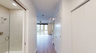 Located at 945 Mid City Dr in Huntsville, Alabama, this efficiently designed unit offers a thoughtful layout across a single floor. The open-concept kitchen and living area serves as the heart of the space, where warm hardwood-style flooring and crisp white walls create a clean, modern aesthetic. A ceiling fan adds both function and style overhead.

The kitchen is well-appointed with light wood cabinetry, white quartz countertops, and a striking geometric tile backsplash. Stainless steel appliances — including a refrigerator with ice maker, electric range, built-in microwave, and dishwasher — are complemented by a matte black gooseneck faucet and open industrial-style shelving, adding a contemporary edge.

The living area is bathed in natural light courtesy of expansive floor-to-ceiling windows that frame views of the surrounding Huntsville cityscape, creating an airy, connected feel despite the compact footprint.

The bathroom features a clean, all-white design with light tile flooring, a wood-accented vanity with a gray countertop, and a glass-enclosed walk-in shower with brushed nickel fixtures. A dedicated closet provides practical storage. The entry hallway connects all rooms with a smooth, efficient flow, reinforcing the unit's well-considered design.