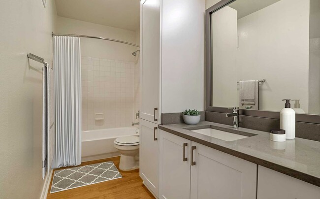 Renovated Package IV bath with white cabinetry, grey quartz countertops, and hard surface plank flooring - Avalon Tysons Corner