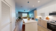 Located at 2990 Longwater Blvd in Kissimmee, FL, this well-designed one-bedroom, one-bathroom residence offers a thoughtfully planned single-level layout with modern finishes throughout. The open-concept kitchen and living area form the heart of the home, where light wood-tone lower cabinetry pairs with crisp white upper cabinets, a tile backsplash, and a full suite of stainless steel appliances including a French door refrigerator, gas range, and built-in microwave. A central island with white countertop and bar seating provides additional prep space and a natural gathering point. The living room features bold teal and gray accent walls, wood-look plank flooring, a ceiling fan, and a large window that brings in natural light and outdoor views. A private entry door with sidelight adds convenience. The bedroom is a calm retreat with a gray accent wall, natural light from dual windows with views of lush greenery, and warm wood flooring. The bathroom connects to a dedicated walk-in closet, complete with built-in shelving and railing. The bathroom itself features a wood-tone vanity, white countertop, a large mirror, and a glass-enclosed shower. The consistent use of natural wood tones, neutral palettes, and modern fixtures gives the entire space a cohesive, contemporary character.