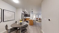 This well-appointed single-floor residence showcases a thoughtfully designed open-concept layout that seamlessly connects the kitchen, dining, and living areas. The kitchen is a standout, featuring two-tone cabinetry with warm wood lower cabinets and dark upper cabinets, white quartz countertops, a classic subway tile backsplash, stainless steel appliances, and a central island with pendant lighting and bar seating — ideal for both cooking and casual entertaining. Light wood-style flooring flows consistently throughout the space, enhancing the bright, airy atmosphere created by the neutral white walls and recessed lighting.

The dining area accommodates a round table with seating for four and sits adjacent to an in-unit washer and dryer. The spacious living room features large windows that invite abundant natural light, a ceiling fan, and direct access to an outdoor area through a glass door. The two bedrooms are comfortably sized with windows offering outdoor views, ceiling fans, and ample room for storage. The bathroom is finished with wood-toned cabinetry, a white countertop vanity, light wood-style flooring, and a walk-in glass-enclosed shower. Throughout, the space maintains a cohesive, contemporary aesthetic with clean lines and a warm, welcoming palette.
