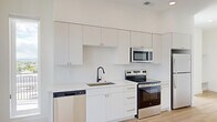 This thoughtfully designed 1-bedroom, 1-bathroom unit offers a clean, contemporary aesthetic throughout its single-floor layout. Light hardwood flooring flows seamlessly across all rooms, complementing the crisp white walls and creating a bright, cohesive atmosphere.

The open-concept kitchen is a standout feature, equipped with a full suite of stainless steel appliances — including a refrigerator, electric range, over-the-range microwave, and dishwasher. Sleek white cabinetry extends to the ceiling, maximizing storage, while white quartz countertops and a matte black faucet add a modern contrast. Recessed lighting enhances the kitchen's clean lines.

The living area benefits from generous natural light, with large sliding glass doors leading to a private balcony that provides open outdoor views, including glimpses of surrounding architecture and distant mountain scenery.

The bedroom is a bright, well-proportioned space featuring a large window that fills the room with natural light and overlooks the surrounding neighborhood. A dedicated closet provides practical storage.

The bathroom is finished to a high standard, showcasing marble-patterned sliding glass shower enclosure walls, light wood cabinetry with a white countertop, a large mirror, and continued hardwood-style flooring. The unit also includes a separate closet, adding to its functional storage capacity.