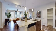 This thoughtfully designed single-floor residence offers a seamless blend of modern style and functional living. The open-concept kitchen serves as the heart of the home, anchored by a large granite-topped island with undermount sink, pendant lighting, and bar seating. Dark wood cabinetry pairs elegantly with stainless steel appliances, including a side-by-side refrigerator, range, and built-in microwave, complemented by a tiled backsplash and track lighting overhead. Rich hardwood flooring flows into the adjacent dining and living areas, where large windows and a glass-panel door flood the space with natural light and offer views of surrounding greenery. The living room features a ceiling fan and ample room for comfortable seating arrangements. Two generously sized bedrooms are finished with plush carpet, ceiling fans, and wide windows dressed with blinds and sheer curtains. Each bedroom connects to a well-appointed bathroom showcasing granite vanity countertops, dark wood cabinetry, and a glass-enclosed walk-in shower with tile surround. The overall ambiance is contemporary and refined, with a neutral color palette, upscale finishes, and a cohesive design language carried consistently throughout the entire residence.