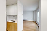 Located at 10155 116 St NW in Edmonton's vibrant Oliver neighbourhood, this one-bedroom, one-bathroom unit offers a clean, modern aesthetic across a thoughtfully laid-out single floor. Light wood laminate flooring runs throughout, lending warmth and visual continuity to every room.

The open living area is bright and airy, benefiting from a large sliding glass door that leads to a private balcony overlooking the surrounding cityscape. Baseboard heating lines the perimeter, ensuring comfort year-round. The kitchen features white upper cabinetry paired with warm wood-toned lower cabinets, a double-basin stainless steel sink with a modern arc faucet, and a clean, minimalist design that integrates seamlessly with the living space.

The bedroom is a well-proportioned, quiet retreat with its own window providing natural light. Two closets offer practical storage solutions, complemented by a central hallway that efficiently connects all areas of the unit. The bathroom is finished with large-format neutral tiles in the shower-tub surround, chrome fixtures, and a wood-accented vanity that echoes the kitchen's design language.

The balcony, accessible from the living area, provides an outdoor extension of the living space with views of the Edmonton skyline. Overall, the unit presents a cohesive, contemporary design with a neutral palette ideal for a variety of living arrangements.