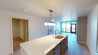 This contemporary single-floor residence offers a well-designed open-concept layout that seamlessly connects the kitchen, dining, and living areas. The kitchen serves as the heart of the home, featuring a large island with a quartz countertop, undermount sink, and pendant lighting above. Warm-toned cabinetry pairs with stainless steel appliances — including a gas range, built-in microwave, and refrigerator — while a classic white subway tile backsplash adds a clean, polished finish. Light wood-tone flooring flows throughout the main living areas, enhancing the bright and airy atmosphere. The spacious living area benefits from floor-to-ceiling windows and direct access to a private balcony, offering sweeping city views and abundant natural light. The bedrooms are generously proportioned, with large windows framing scenic outdoor vistas; the primary bedroom includes a ceiling fan and an oversized window with panoramic views. Both bathrooms are finished with quartz vanity countertops, warm wood cabinetry, built-in shelving, and a combination tub/shower. A dedicated in-unit laundry room with side-by-side washer and dryer and overhead wire shelving adds everyday convenience to this thoughtfully designed residence.