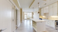 Located at 7511 Solstice Cir in Orlando, Florida, this 1-bedroom, 2-bathroom residence offers a thoughtfully designed single-floor layout with a bright, open-concept living space. The kitchen is a standout feature, showcasing white shaker cabinetry with glass-front uppers, a decorative arabesque tile backsplash, stainless steel appliances including a range with a sleek hood vent and a French door refrigerator, and a large center island with built-in shelving and a crisp white countertop. Antique brass pendant lights add a warm, stylish touch overhead. Light hardwood-style flooring flows throughout the main living and kitchen areas, while the bedroom features plush carpeting for added comfort. Large windows with blinds allow abundant natural light and offer views of the surrounding neighborhood. The primary bedroom is generously proportioned and connects to a well-appointed en-suite bathroom with a vanity, tile flooring, and a glass-enclosed shower, alongside a dedicated walk-in closet with wire shelving. The unit also includes a utility room, in-unit laundry, and access to a private balcony. Crown molding and a neutral warm-beige color palette give the space a clean, cohesive aesthetic throughout.