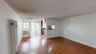 Located on the second floor at 21431 Saticoy St in Canoga Park, CA, this one-bedroom, one-bathroom unit offers a practical and comfortable layout across a single level. The combined kitchen and living area serves as the heart of the home, with rich hardwood-style flooring adding warmth throughout. The kitchen is well-equipped, featuring deep-toned wood cabinetry, dark granite countertops, a tile backsplash, a gas range, and a stainless steel sink beneath a window that brings in natural light — all set on clean ceramic tile flooring. The living area provides an open, versatile space ideal for everyday living. A hallway connects the main living space to the private quarters. The bedroom is carpeted for comfort and features mirrored sliding closet doors that enhance the sense of space, along with a window that allows natural light and outdoor views to filter in. The full bathroom includes a clean, white tub-shower combination. A private balcony overlooks a landscaped courtyard with tropical foliage and views of the surrounding building, offering a pleasant outdoor retreat. Textured ceilings are consistent throughout the unit, and the neutral color palette creates a bright, cohesive ambiance throughout the home.