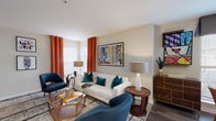 This single-floor residence combines contemporary finishes with mid-century modern design sensibilities to create a cohesive and vibrant living environment. The living room serves as the heart of the space, featuring wood-look flooring, a white-mantled fireplace, and bold pop-art wall pieces that add visual interest. Large windows dressed with rich orange curtains invite natural light throughout, while built-in shelving flanks the fireplace for added functionality.

The dining area accommodates a round table surrounded by natural light from multiple windows, creating a bright and welcoming setting. The galley-style kitchen is outfitted with stainless steel appliances, wood-grain cabinetry, and white quartz countertops, offering an efficient and modern workspace.

Both bedrooms feature plush carpeting and generous natural light. The primary bedroom includes a large dresser with a mirror and direct access to additional rooms, while the secondary bedroom offers a walk-in closet. The bathroom presents tile flooring, a tub-shower combination with full tile surround, and contemporary gray cabinetry. A dedicated in-unit laundry room with full-size washer and dryer and overhead shelving completes this well-appointed residence.