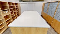 This 350-square-foot package room, situated at 150 Broad St in Windsor, CT, is a testament to modern functionality and design. The space is efficiently organized with an extensive wall of mailboxes, providing individual compartments for residents. A central island with a pristine white countertop serves as a sorting area, complemented by warm wood tones that add a touch of elegance to the utilitarian space.

Illumination is thoughtfully implemented with recessed lighting and stylish pendant lamps, ensuring the area is well-lit for easy navigation. The room's layout includes open shelving units, offering additional storage for larger parcels. The entryway features glass doors that allow natural light to flood in, creating an inviting atmosphere. A decorative mirror and potted plants near the entrance add a welcoming touch.

The room's design prioritizes accessibility, with clear pathways and a spacious layout. High ceilings with drop tiles contribute to a sense of openness. The polished concrete flooring adds a contemporary feel while providing durability for high-traffic use. This package room exemplifies a perfect blend of practicality and aesthetic appeal, serving as an essential amenity for the building's residents.
